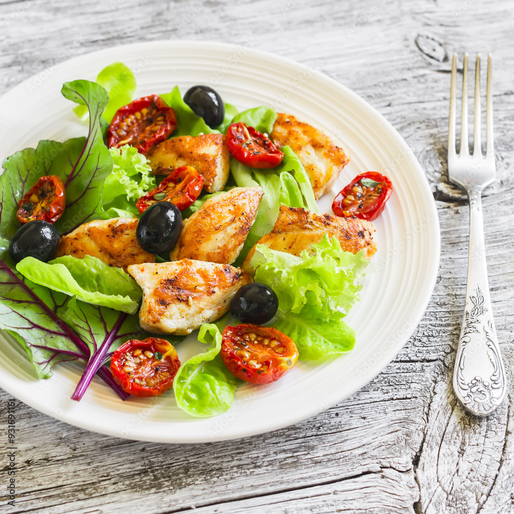 Fresh salad with chicken breast, sun-dried tomatoes, green salad and olives on a white plate on a wooden surface. Healthy food Fresh salad with chicken breast, sun-dried tomatoes, green salad and olives on a white plate on a wooden surface. Healthy food