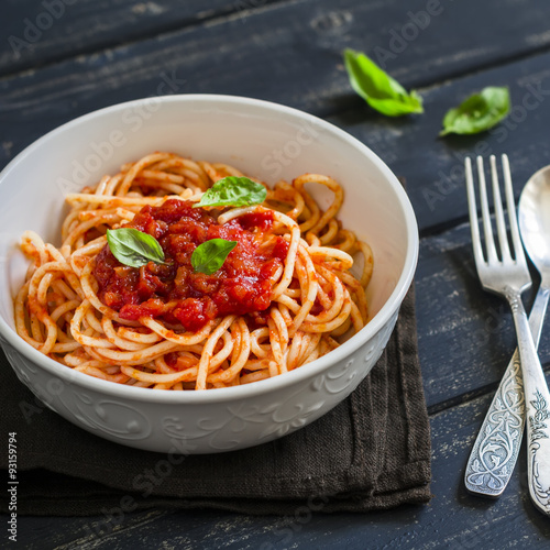 spaghetti with tomato sauce and Basil in a white bowl on a dark wooden surface