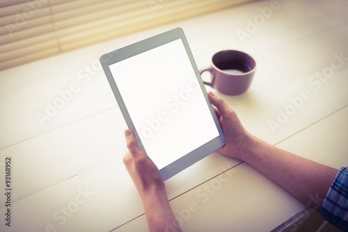  Hands holding digital tablet by coffee cup on table