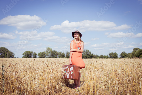 Young beautiful lady in orange dress holding old valise in field photo