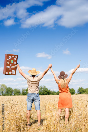 Happy exciting couple with valise rising hands together in wheat