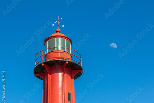 A lighthouse and the moon against blue sky