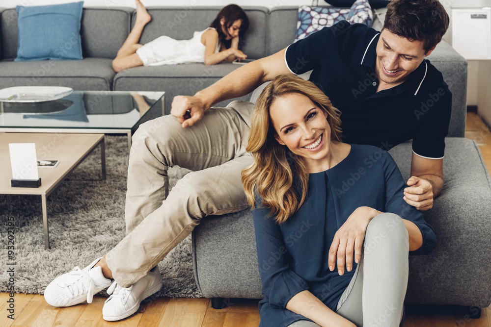 Smiling couple in living room with daughter using digital tablet in background Smiling couple in living room with daughter using digital tablet in background