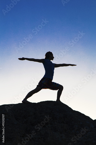 Young lady in yoga position on the rocks on sunset light