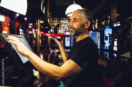 Waiter holding tray with beverages in an Irish pub while operating at till photo