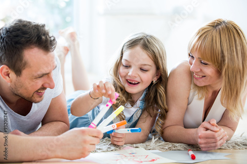 Little girl lying on floor with parents, drawing with felt tip pens