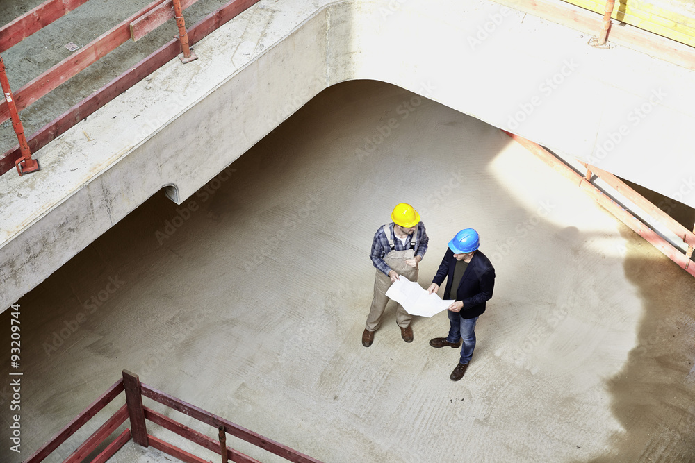 Construction worker and architect with plan talking on construction site Construction worker and architect with plan talking on construction site