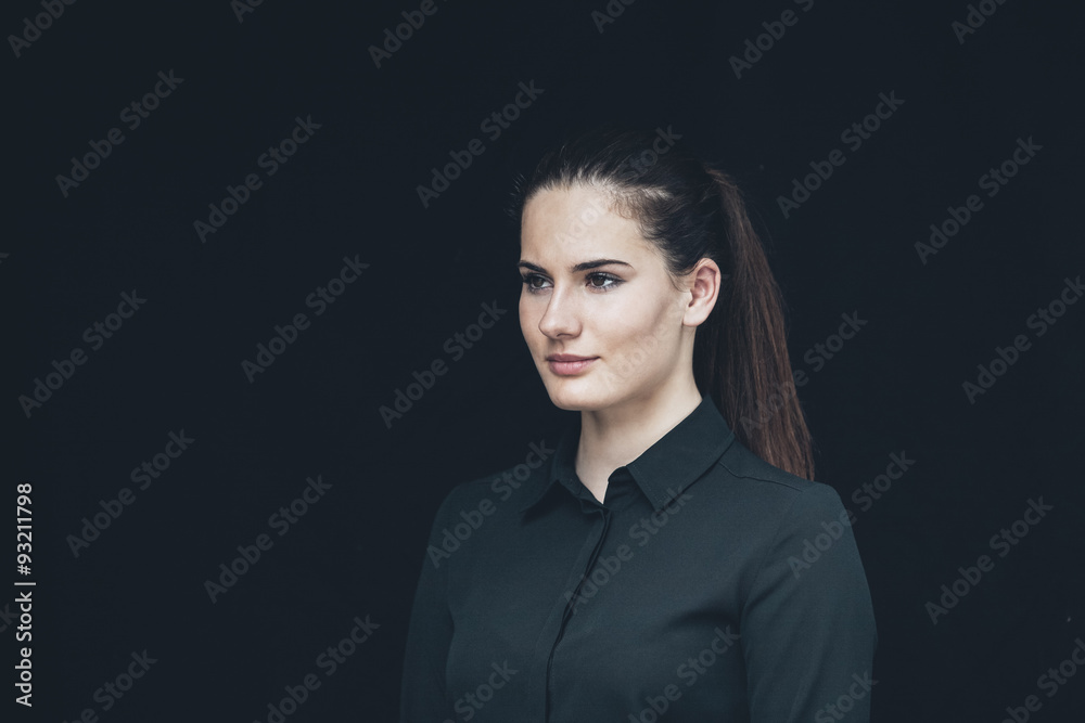 Portrait of young woman with ponytail in front of black background