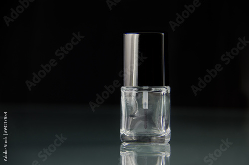 Empty nail polish makeup bottle with no label with a shiny glass reflection against a dark background with dramatic lighting.