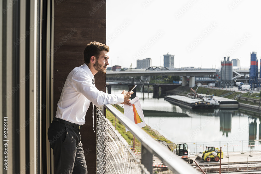 Young businessman standing on balcony looking at view Young businessman standing on balcony looking at view