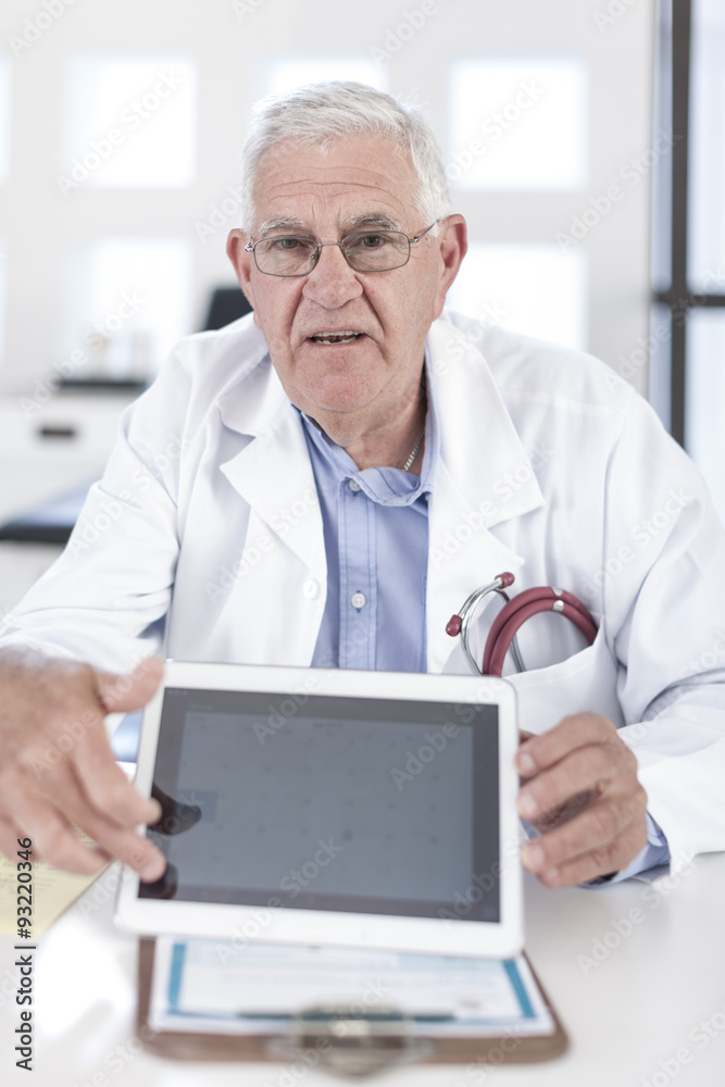 Serious senior doctor at desk showing digital tablet Serious senior doctor at desk showing digital tablet