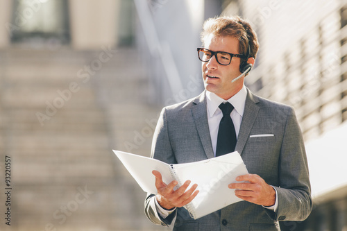 Businessman outdoors wearing headset discussing file photo