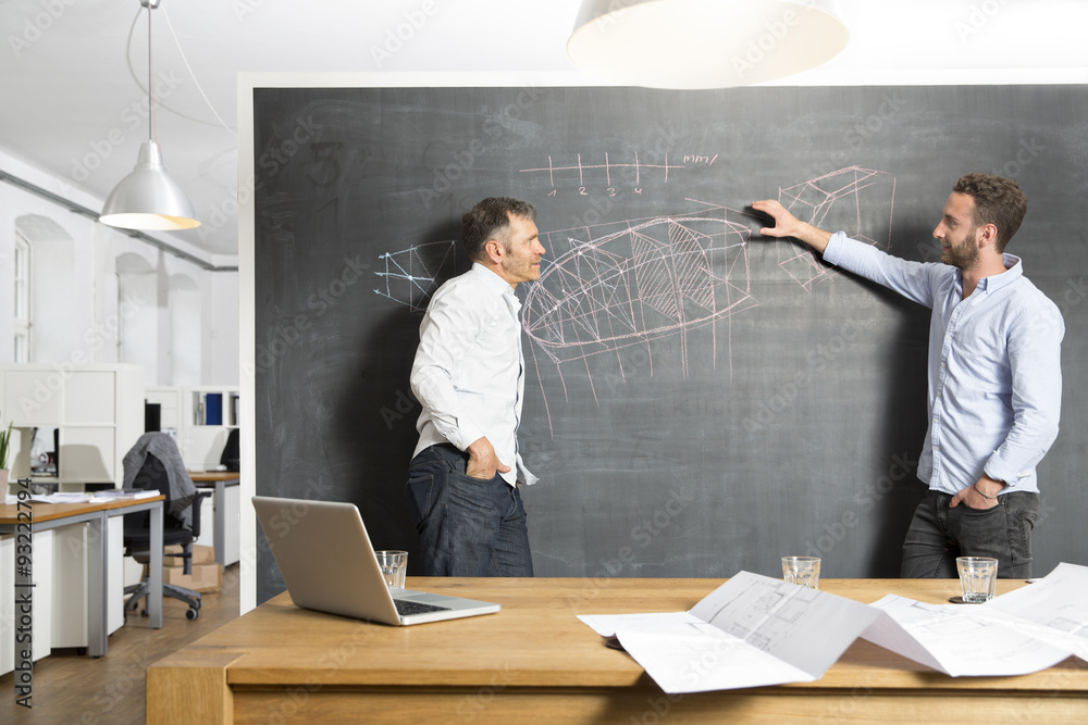 Two businessmen discussing drawing at blackboard Two businessmen discussing drawing at blackboard