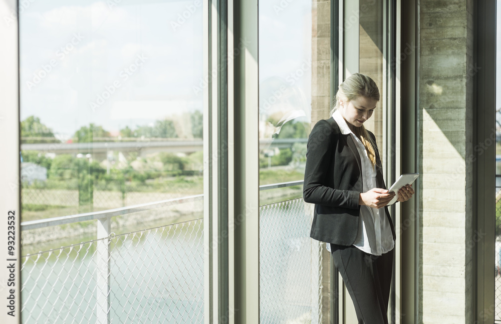 Young businesswoman at the window looking on digital tablet
