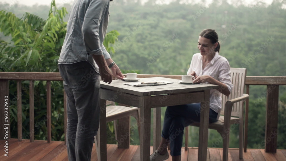 Young couple talking and drinking coffee by table on terrace
Young couple talking and drinking coffee by table on terrace