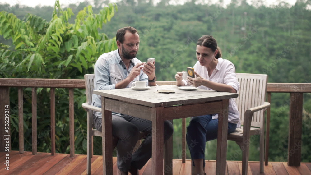 Young couple using smartphone and drinking coffee by table on terrace
Young couple using smartphone and drinking coffee by table on terrace