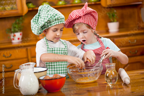 two children preparing eggs for cookies in the kitchen