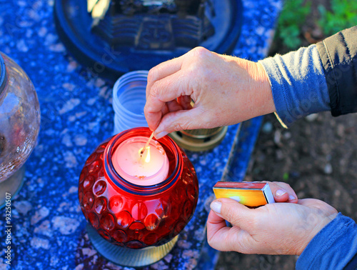 Woman at cemetery is lighting a red candle