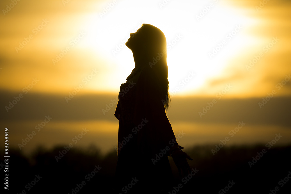 Twilight silhouette by beautiful sunny young woman in summer. The sun stands at the horizon and the girl becomes a very nice black silhouette