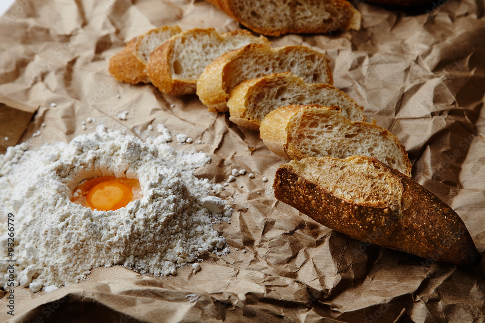 Sliced baguette and egg in flour bowl on craft paper