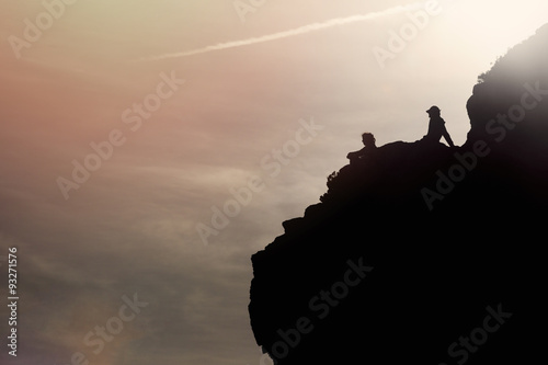 people silhouettes sitting on the rock at sunset