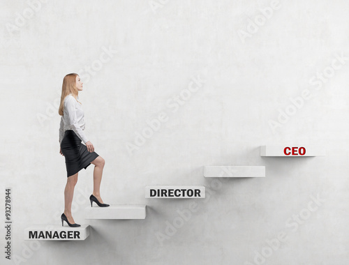 A young business lady is going up the corporate ladder from the manager to CEO. Concrete background.