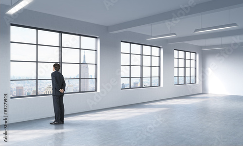 A full length man in formal suit who is looking out the window, New York panoramic view. A modern loft style open space.