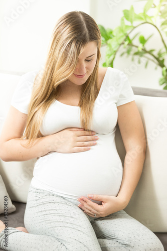 Free Download smiling expectant mother relaxing on sofa and looking on tummy - GFXLoad