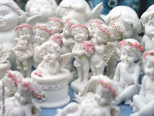 Group of cute baby angels statues with pink roses wreaths on their heads. 