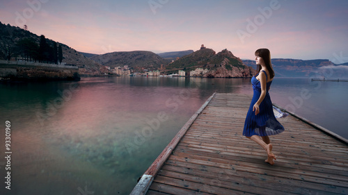 Fairy woman in dress on the dock by the sea on a background of mountains.