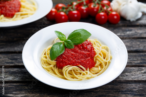 Spaghetti with marinara sauce and basil leaves on top, decorated with vegetables. on wooden table.