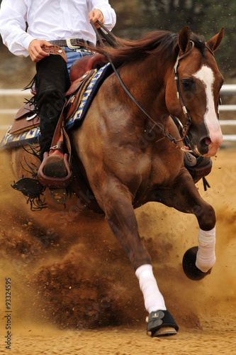 A front view of a rider and horse sliding in the dust. © PROMA