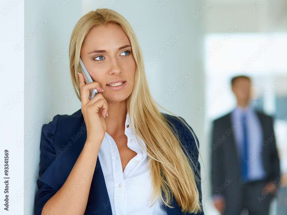 Businesswoman standing against office window talking on mobile Businesswoman standing against office window talking on mobile