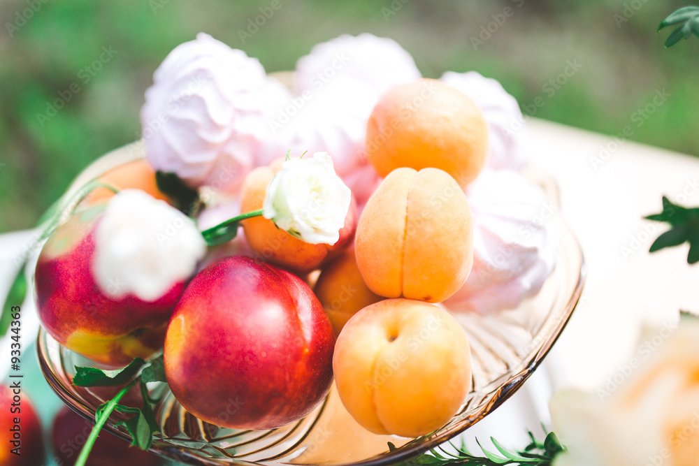 Ripe peaches in in a glass bowl for fruits on the table with marshmallow