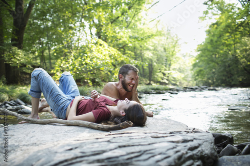 A young man and woman lying on the rocks on a river bank. photo