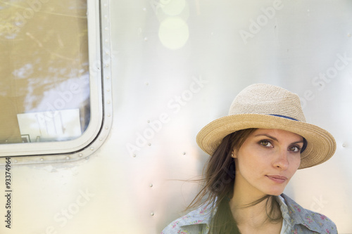 A young woman wearing a hat sitting in the shade of a silver coloured trailer. photo
