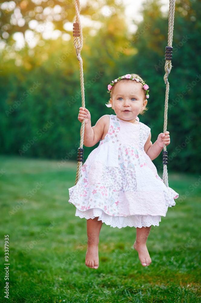 Adorable baby girl enjoying a swing ride on a playground in a park Adorable baby girl enjoying a swing ride on a playground in a park