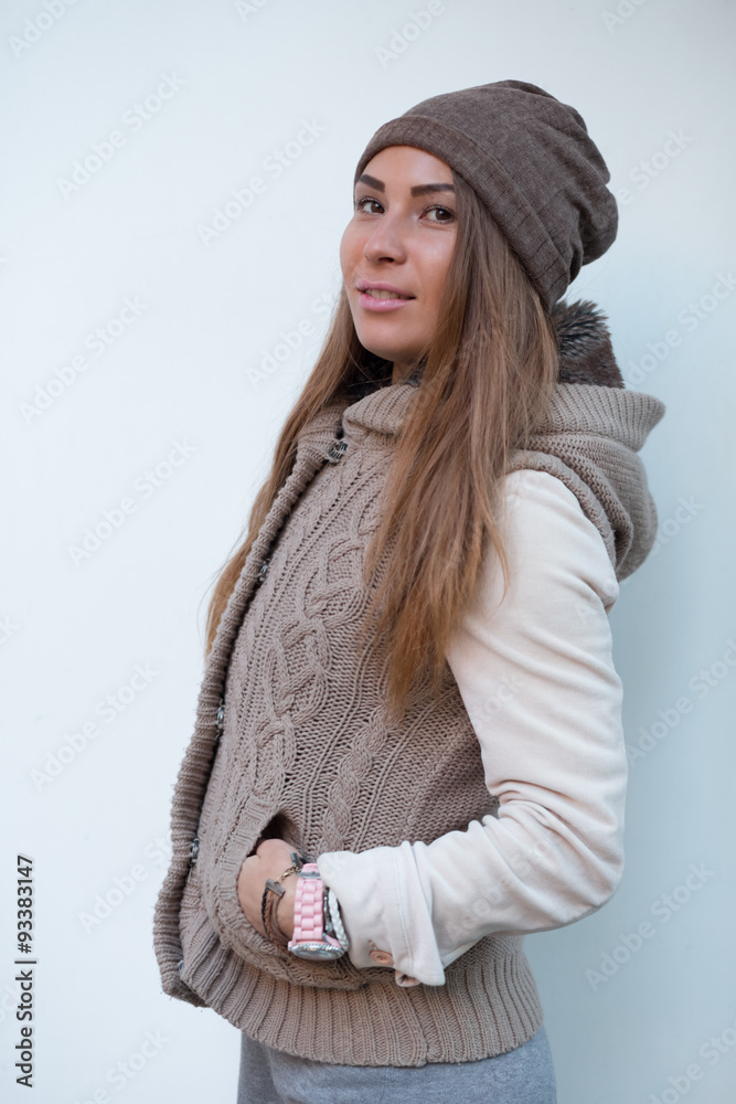 Beautiful woman in knitted garment and cap near white wall
