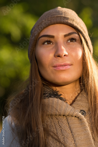 Beautiful woman in a knitted garment and cap in the park. Close up portrait.