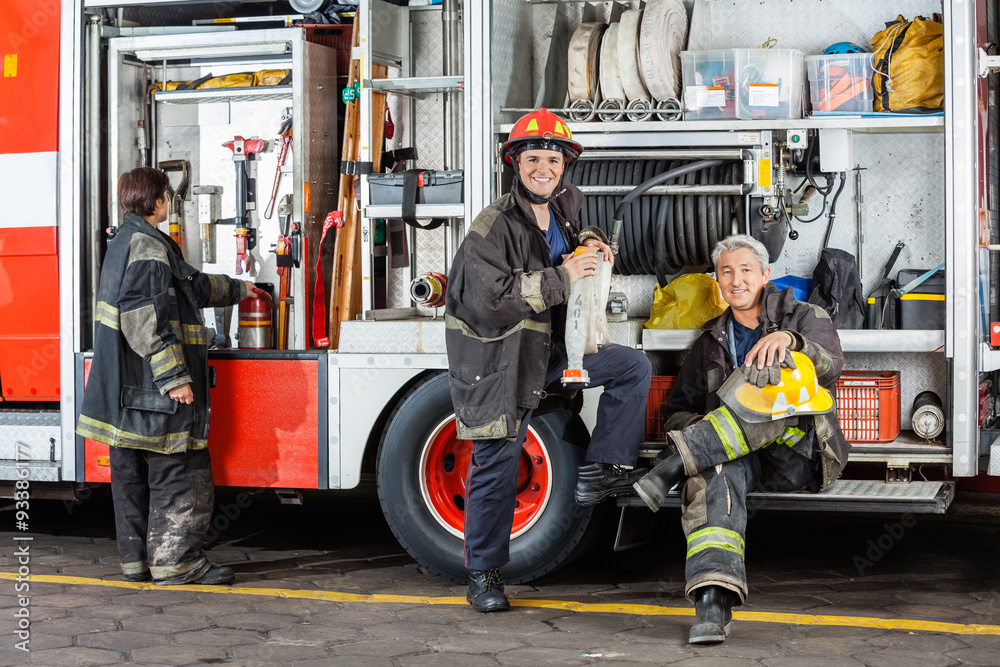 Confident Firefighters By Truck At Fire Station Confident Firefighters By Truck At Fire Station