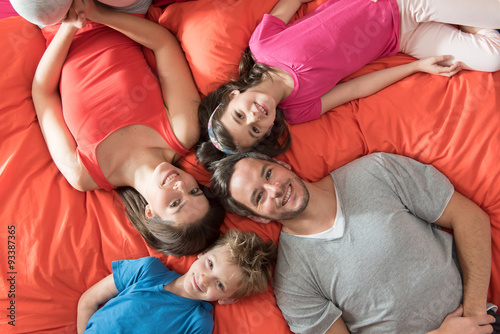 top view of a four people family laying on their big red bed 