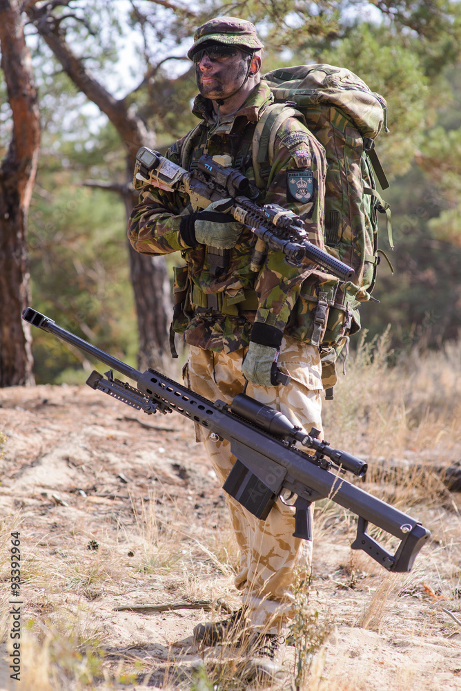 Special forces soldier with painted fase and sniper rifle in forest