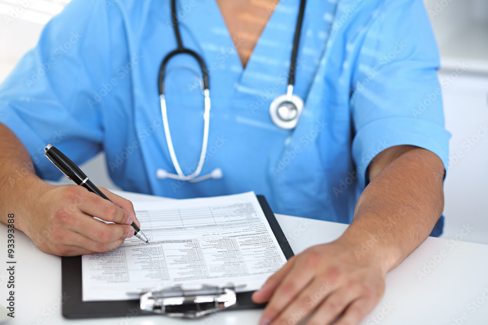 Portrait of unknown male surgeon doctor holding his stethoscope and filling up medical history Portrait of unknown male surgeon doctor holding his stethoscope and filling up medical history