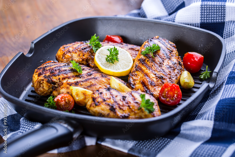 Grilled chicken breast in different variations with cherry tomatoes, green French beans, garlic, herbs, cut lemon on a wooden board or teflon pan. Traditional cuisine. Grill kitchen. Grilled chicken breast in different variations with cherry tomatoes, green French beans, garlic, herbs, cut lemon on a wooden board or teflon pan. Traditional cuisine. Grill kitchen.