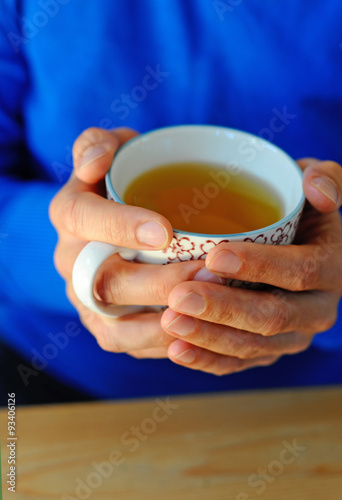 Mann wärmt seine Hände an einer Tasse Tee