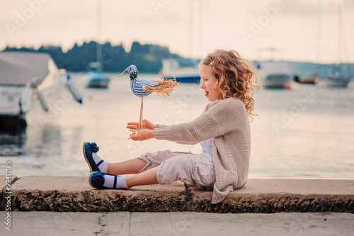 child girl playing with toy bird on sea side on summer vacation photo