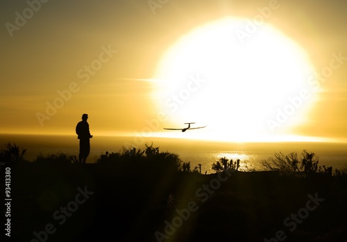 person flying toy plane over ocean with sun setting in the background