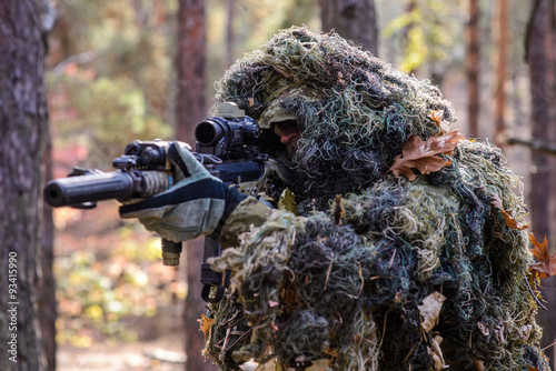 Armed sniper in camouflage suit/Armed man in camouflage suit aiming a sniper rifle in forest