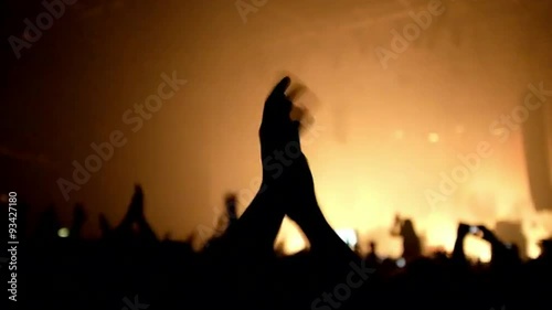 Here is  footage of people crowd partying at a concert or a night club. You can see dark silhouettes dancing, jumping and waving hands in front of stage.