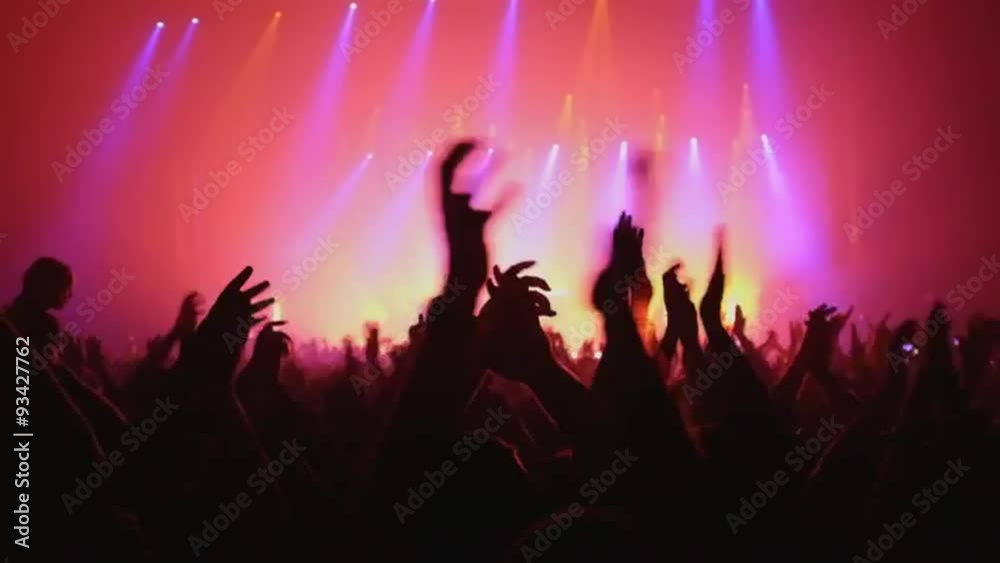 Here is  footage of people crowd partying at a concert or a night club. You can see dark silhouettes dancing, jumping and waving hands in front of stage.